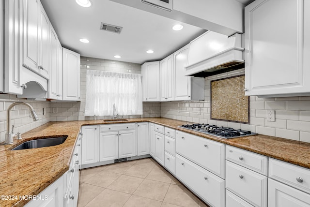 kitchen featuring white cabinets, light stone counters, stainless steel gas stovetop, and sink