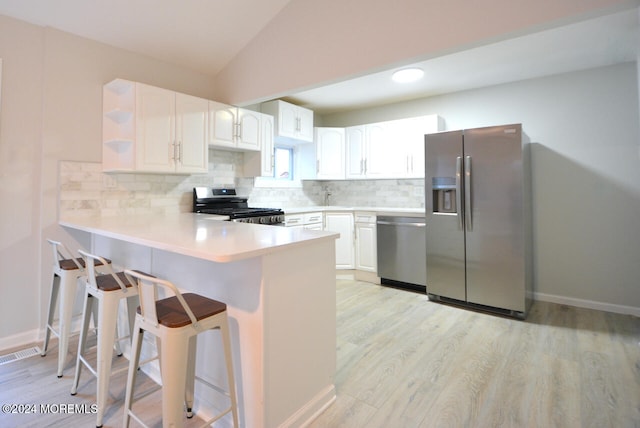 kitchen featuring light wood-type flooring, tasteful backsplash, white cabinetry, kitchen peninsula, and stainless steel appliances