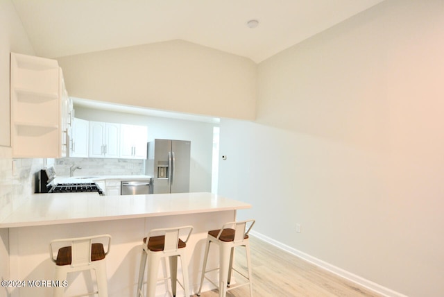 kitchen featuring decorative backsplash, appliances with stainless steel finishes, light wood-type flooring, vaulted ceiling, and white cabinetry