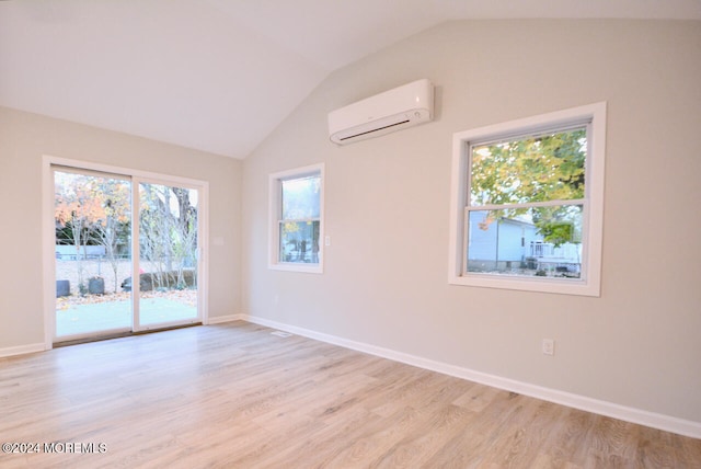 empty room featuring plenty of natural light, light hardwood / wood-style floors, a wall unit AC, and vaulted ceiling