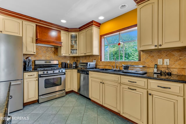 kitchen featuring appliances with stainless steel finishes, light tile patterned floors, dark stone counters, and sink