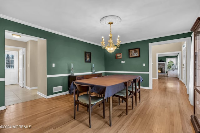 dining area with a notable chandelier, light hardwood / wood-style floors, crown molding, and a fireplace