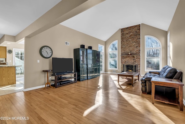 living room with light hardwood / wood-style floors, vaulted ceiling, sink, and a brick fireplace