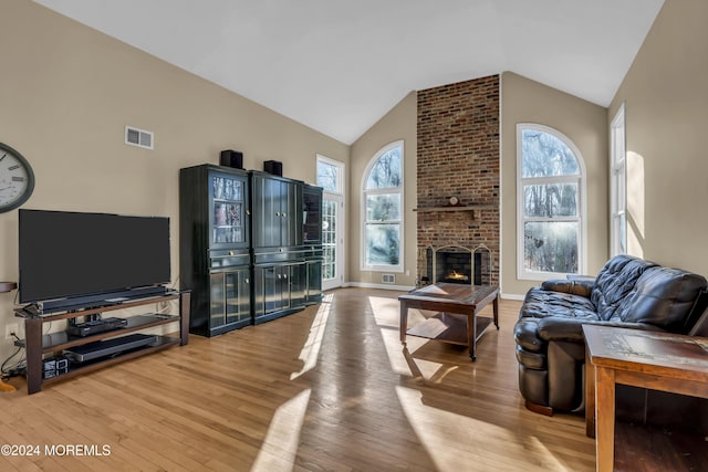 living room with a brick fireplace, high vaulted ceiling, and light wood-type flooring