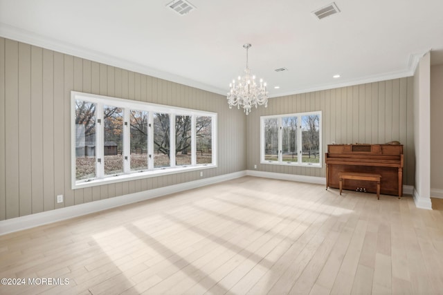 interior space with wood walls, an inviting chandelier, crown molding, and light hardwood / wood-style flooring