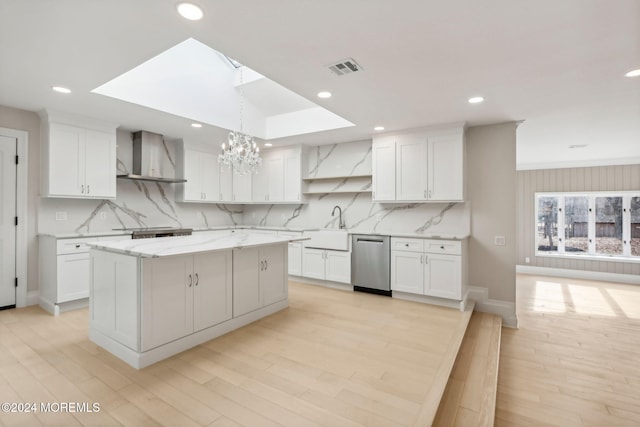 kitchen with white cabinets, a skylight, wall chimney exhaust hood, and dishwasher