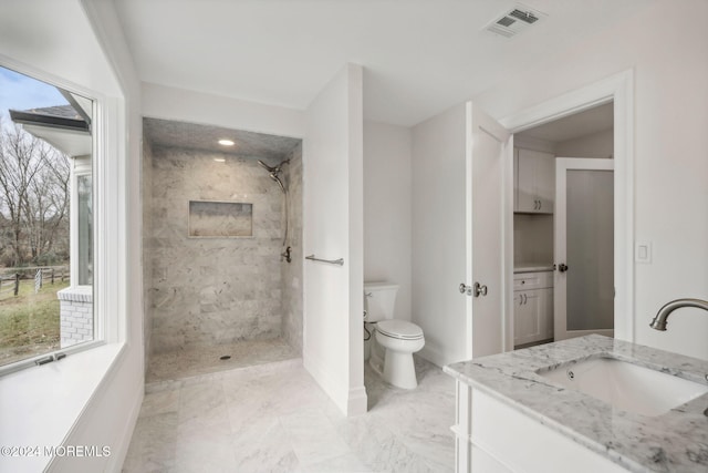 bathroom featuring a tile shower, a wealth of natural light, vanity, and toilet