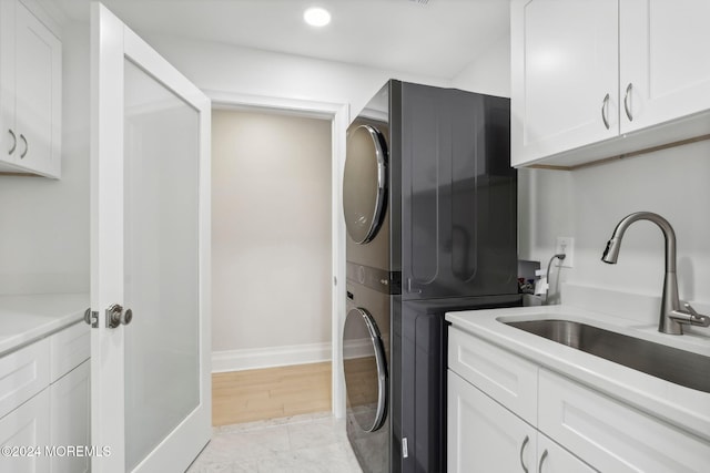 clothes washing area with cabinets, light wood-type flooring, stacked washer / drying machine, and sink