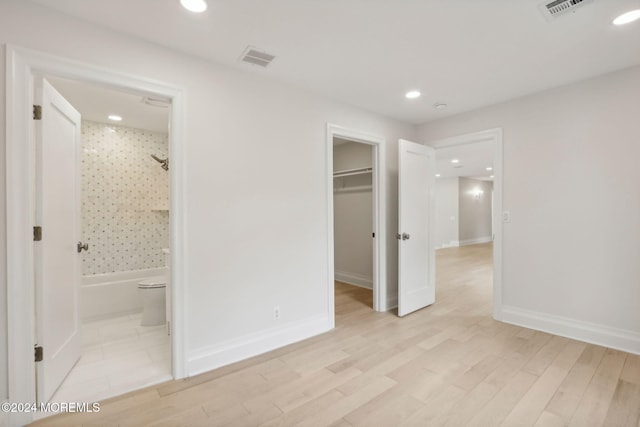 unfurnished bedroom featuring connected bathroom, a spacious closet, a closet, and light hardwood / wood-style floors