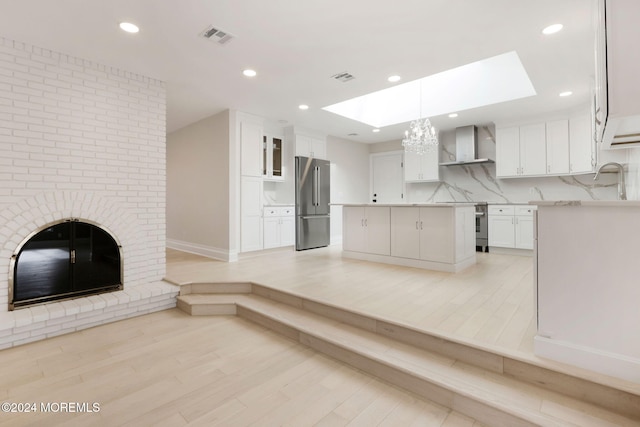 kitchen with stainless steel fridge, light wood-type flooring, wall chimney range hood, white cabinets, and a kitchen island