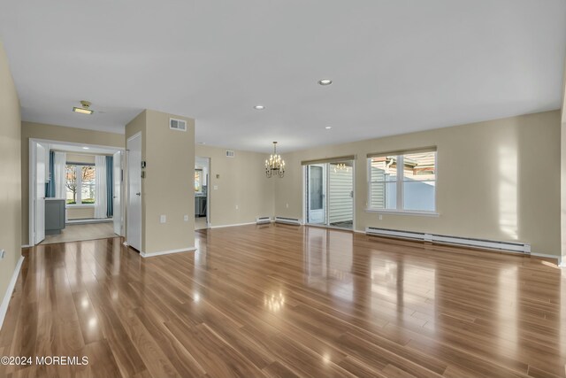 unfurnished living room featuring a notable chandelier, wood-type flooring, and baseboard heating