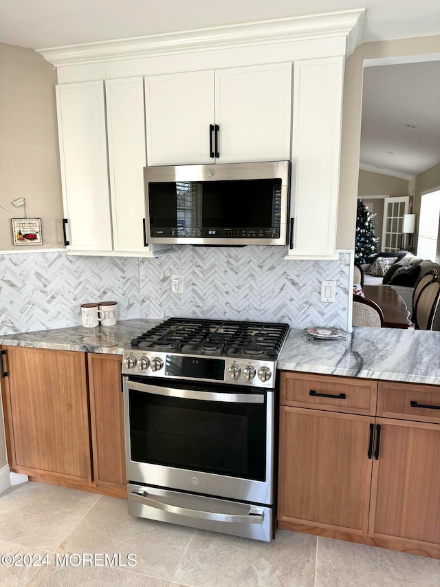 kitchen with vaulted ceiling, light tile patterned floors, appliances with stainless steel finishes, tasteful backsplash, and white cabinetry