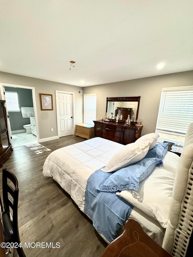 bedroom with multiple windows, ensuite bath, and dark hardwood / wood-style floors