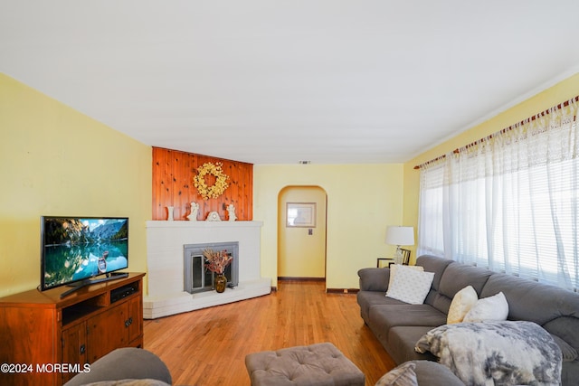 living room with wooden walls, light hardwood / wood-style flooring, and a brick fireplace