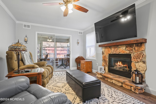 living room with hardwood / wood-style floors, a stone fireplace, ceiling fan, and ornamental molding