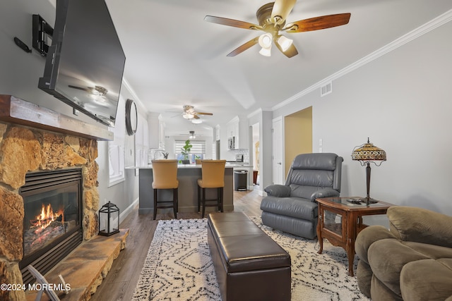 living room featuring dark hardwood / wood-style floors, a stone fireplace, ceiling fan, and ornamental molding