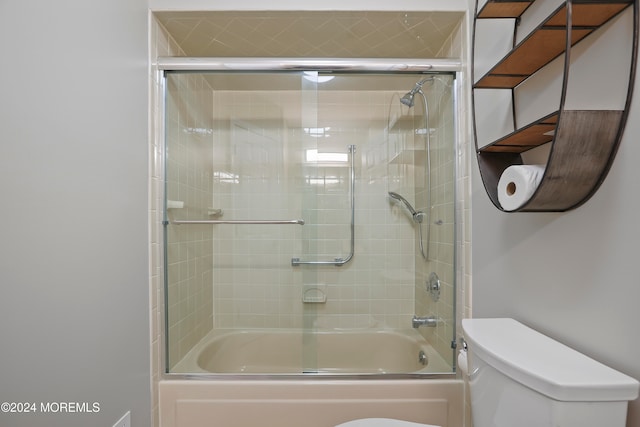 bathroom featuring toilet and shower / bath combination with glass door