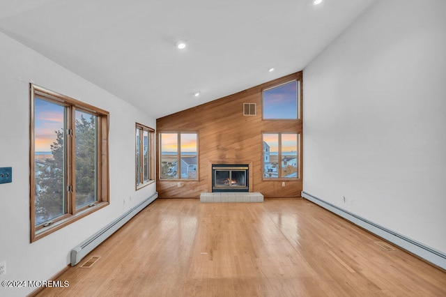 unfurnished living room with light wood-type flooring, wooden walls, and a baseboard radiator