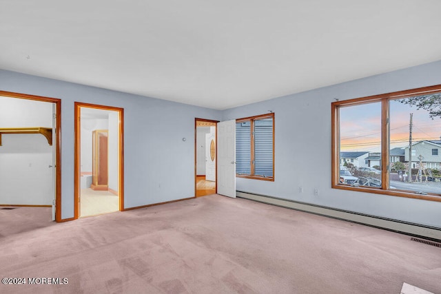 unfurnished bedroom featuring ensuite bathroom, light colored carpet, and a baseboard heating unit