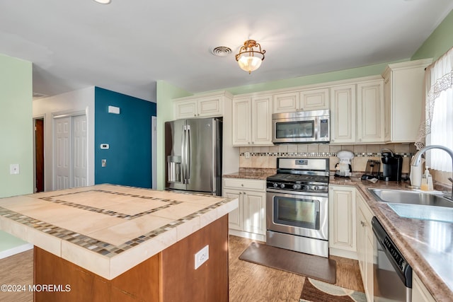 kitchen featuring sink, a kitchen island, appliances with stainless steel finishes, tasteful backsplash, and light hardwood / wood-style floors