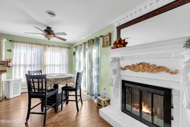 dining room with a fireplace, hardwood / wood-style floors, ceiling fan, and a baseboard heating unit