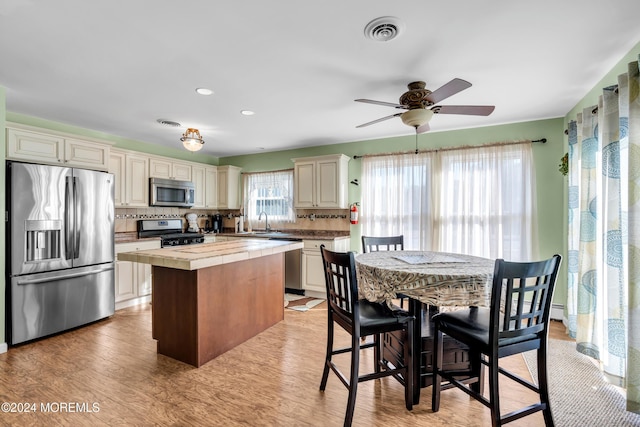 kitchen with appliances with stainless steel finishes, sink, tile countertops, a center island, and light hardwood / wood-style floors