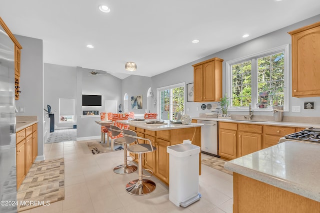 kitchen featuring sink, stainless steel appliances, a kitchen island, light brown cabinetry, and light tile patterned flooring