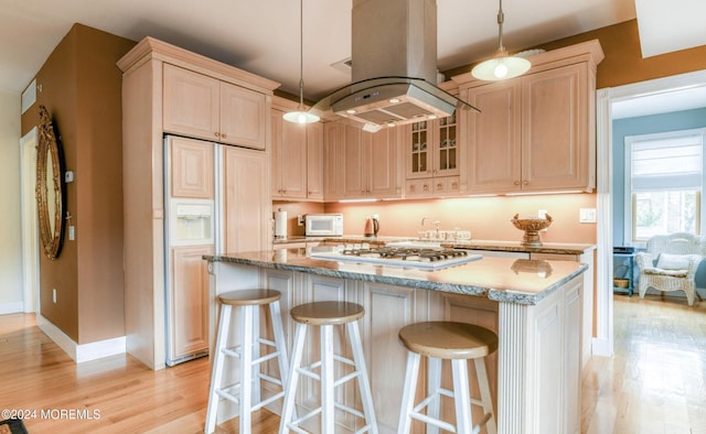 kitchen with island exhaust hood, light stone counters, stainless steel gas cooktop, paneled built in refrigerator, and hanging light fixtures