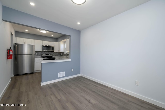 kitchen featuring backsplash, white cabinets, kitchen peninsula, wood-type flooring, and stainless steel appliances