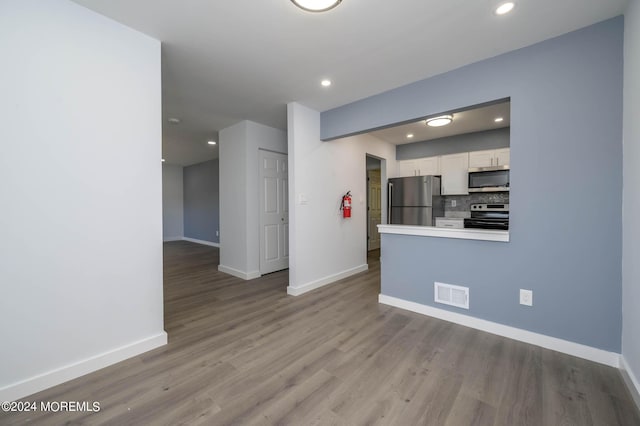 kitchen with white cabinets, decorative backsplash, light wood-type flooring, and stainless steel appliances