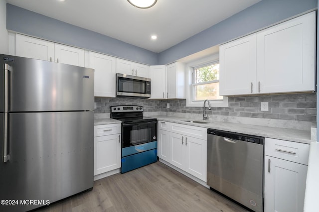 kitchen with backsplash, sink, light hardwood / wood-style flooring, appliances with stainless steel finishes, and white cabinetry