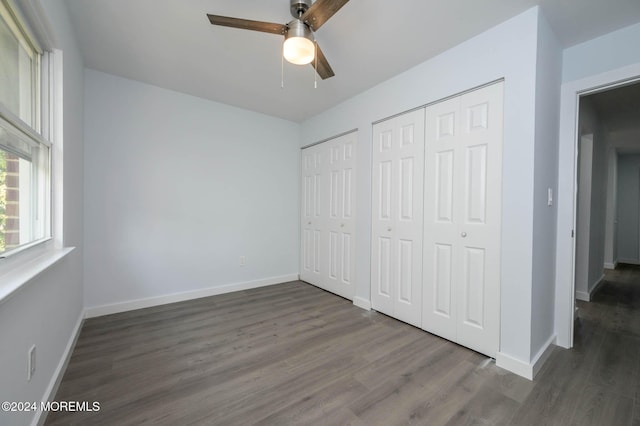 unfurnished bedroom with ceiling fan, dark wood-type flooring, and two closets