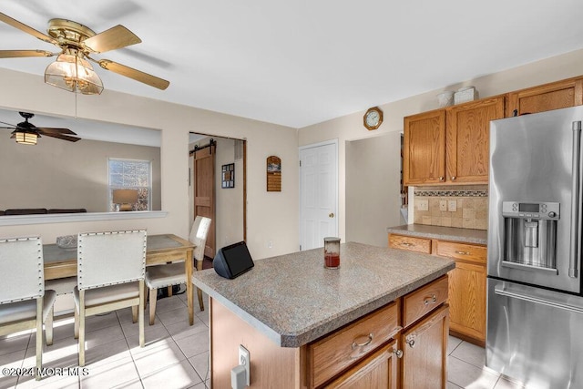 kitchen featuring a center island, ceiling fan, light tile patterned floors, tasteful backsplash, and stainless steel fridge with ice dispenser