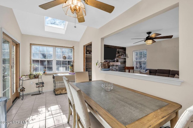 tiled dining space featuring lofted ceiling with skylight and ceiling fan