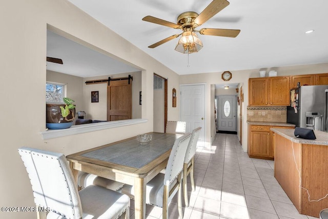 tiled dining space featuring ceiling fan and a barn door