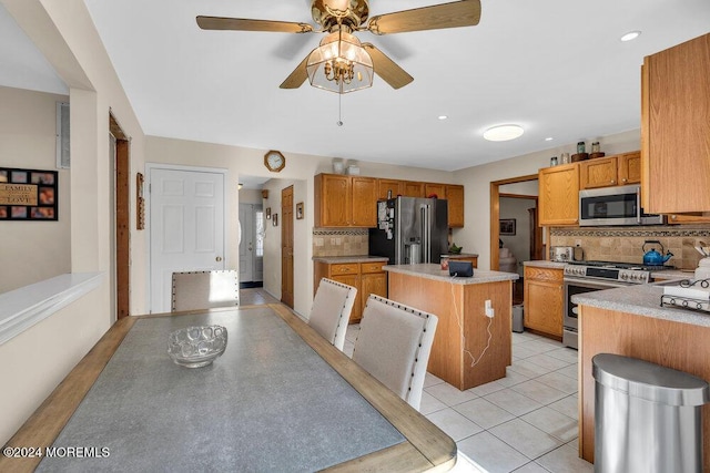 kitchen with decorative backsplash, ceiling fan, light tile patterned floors, a kitchen island, and stainless steel appliances