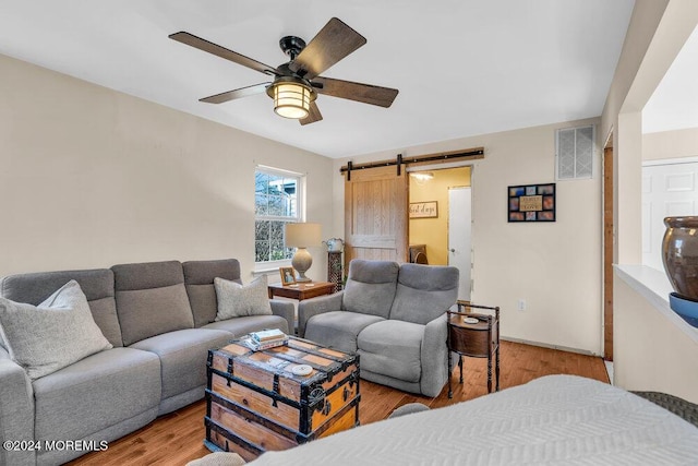 living room with a barn door, ceiling fan, and light hardwood / wood-style flooring