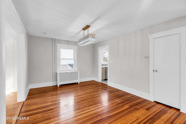 empty room featuring radiator, hardwood / wood-style floors, and an inviting chandelier