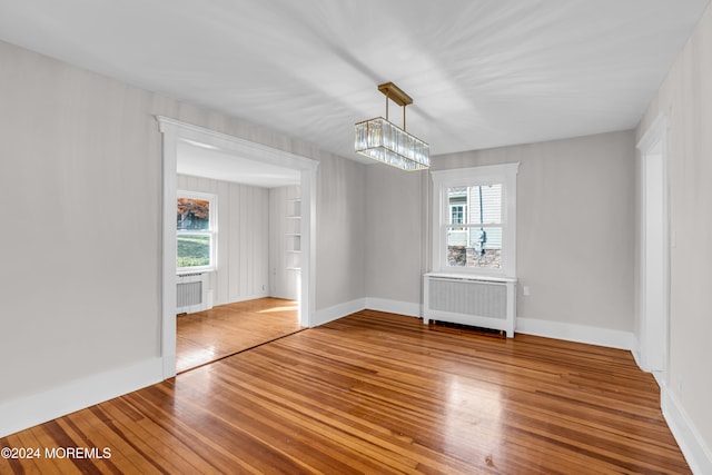 empty room featuring wood-type flooring, an inviting chandelier, and radiator