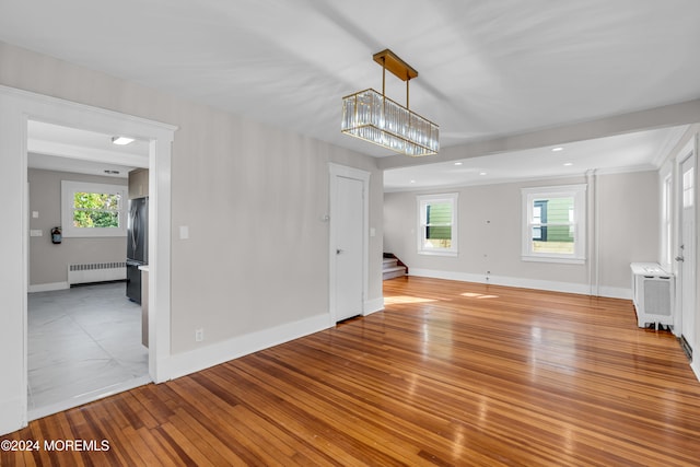 unfurnished living room featuring radiator, a chandelier, and light hardwood / wood-style floors