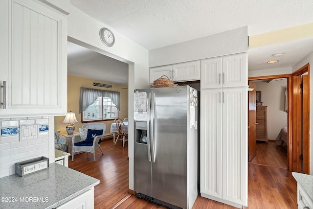 kitchen with light stone countertops, stainless steel fridge, tasteful backsplash, white cabinets, and light hardwood / wood-style floors