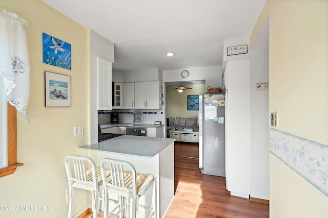 kitchen with kitchen peninsula, ceiling fan, dark wood-type flooring, white cabinets, and stainless steel refrigerator