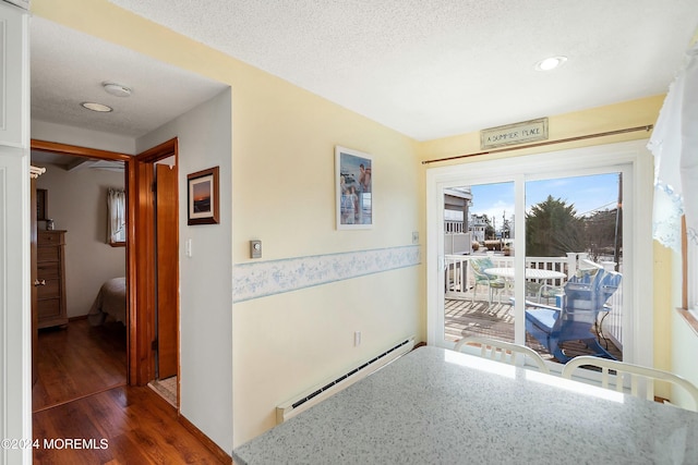 hall with a textured ceiling, dark hardwood / wood-style floors, and a baseboard heating unit