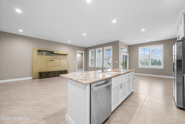 kitchen with a center island with sink, white cabinets, sink, light stone counters, and stainless steel appliances