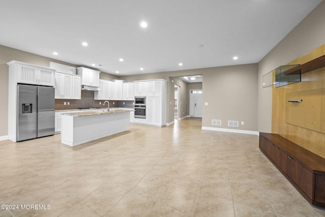 kitchen featuring backsplash, a kitchen island with sink, white cabinets, appliances with stainless steel finishes, and light stone counters