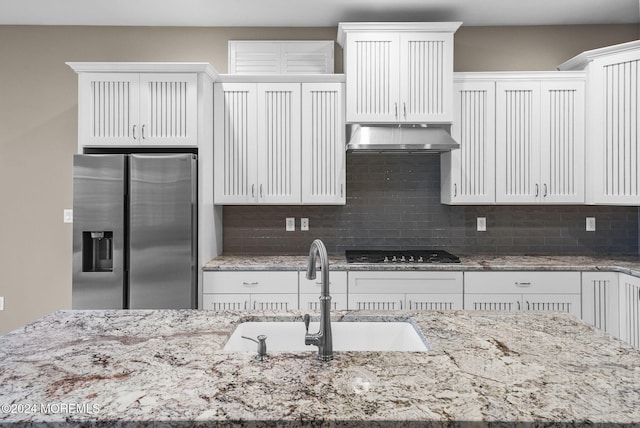 kitchen featuring black gas stovetop, sink, stainless steel refrigerator with ice dispenser, light stone countertops, and white cabinetry