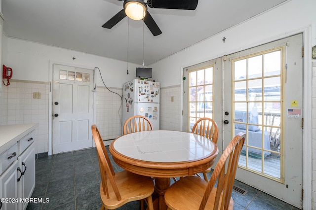 dining area featuring dark tile patterned flooring, tile walls, and ceiling fan