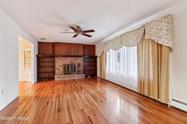 unfurnished living room featuring ceiling fan, a brick fireplace, baseboard heating, wood walls, and hardwood / wood-style floors