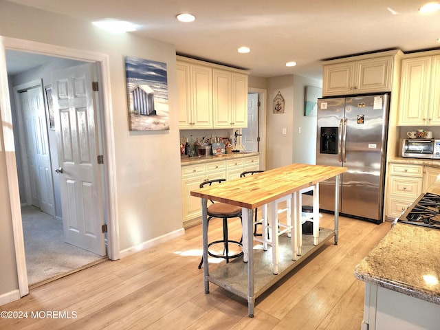 kitchen featuring cream cabinetry, light hardwood / wood-style floors, light stone counters, and appliances with stainless steel finishes