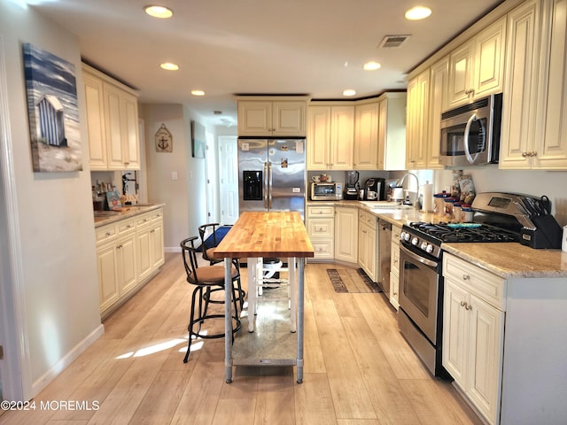 kitchen with cream cabinets, sink, light hardwood / wood-style flooring, butcher block countertops, and stainless steel appliances